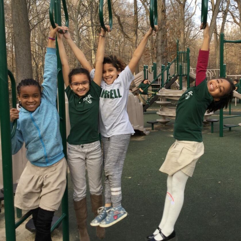 Students Enjoying Recess at Farrell Elementary Four smiling students from Farrell Elementary hang from playground equipment surrounded by trees during recess.